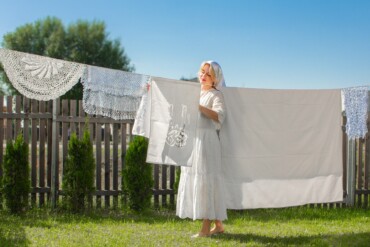 Beautiful young woman with blonde hair hanging and drying her clean white laundry on rope