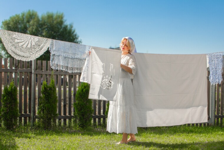 Beautiful young woman with blonde hair hanging and drying her clean white laundry on rope