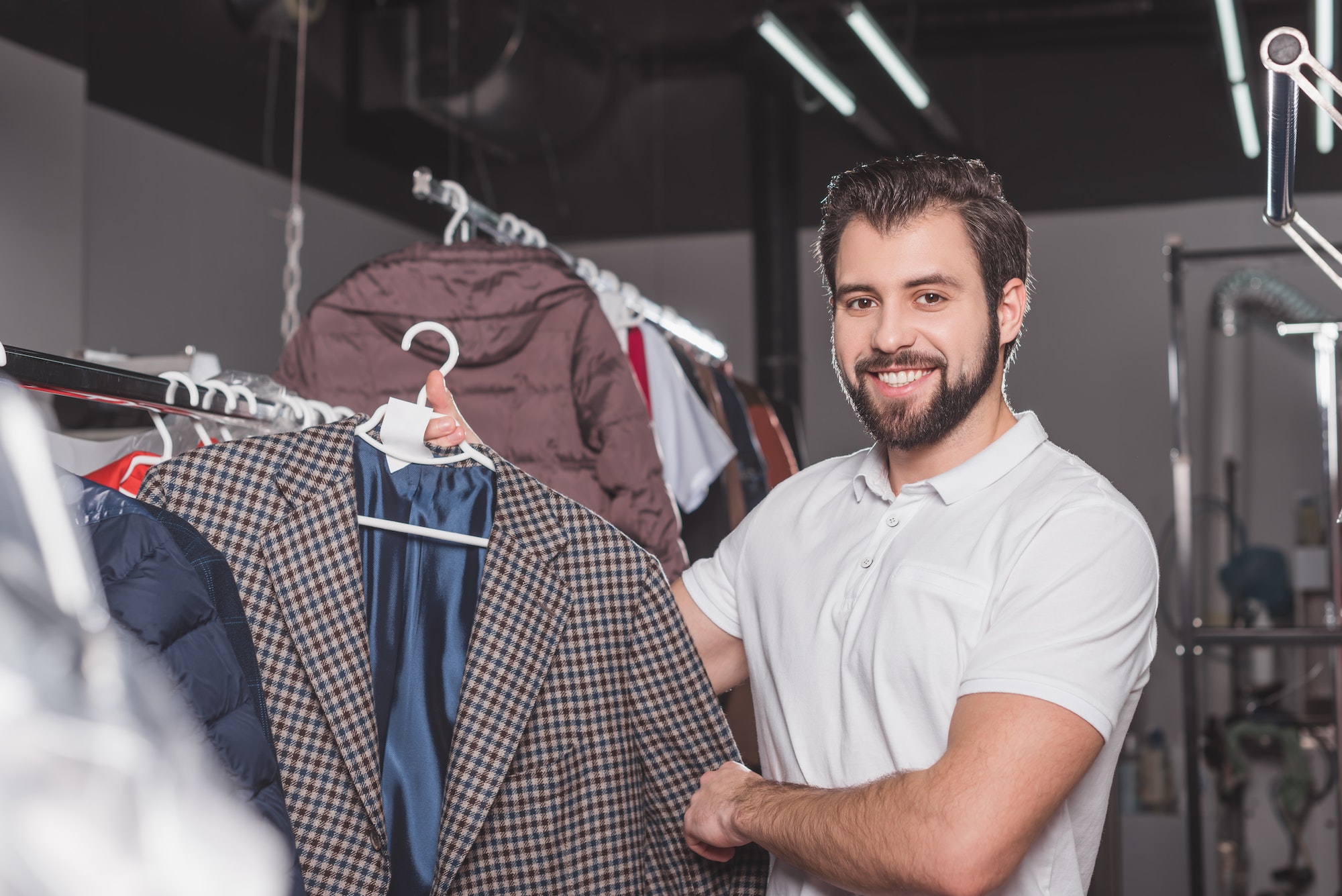 happy young dry cleaning worker hanging jacket at warehouse