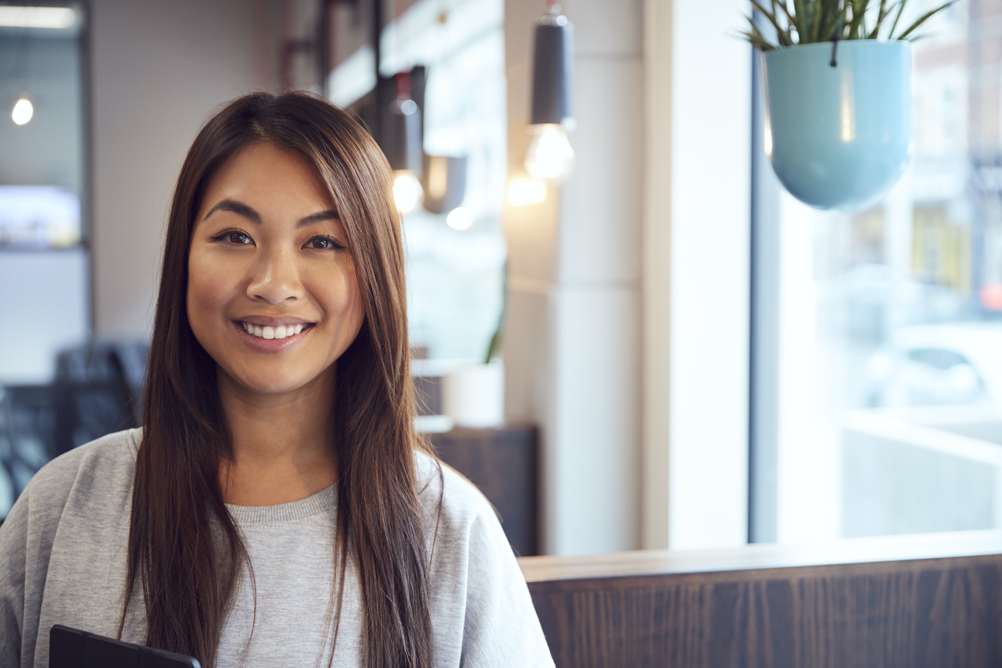 Head And Shoulders Portrait Of Smiling Young Asian Businesswoman Working In Modern Office