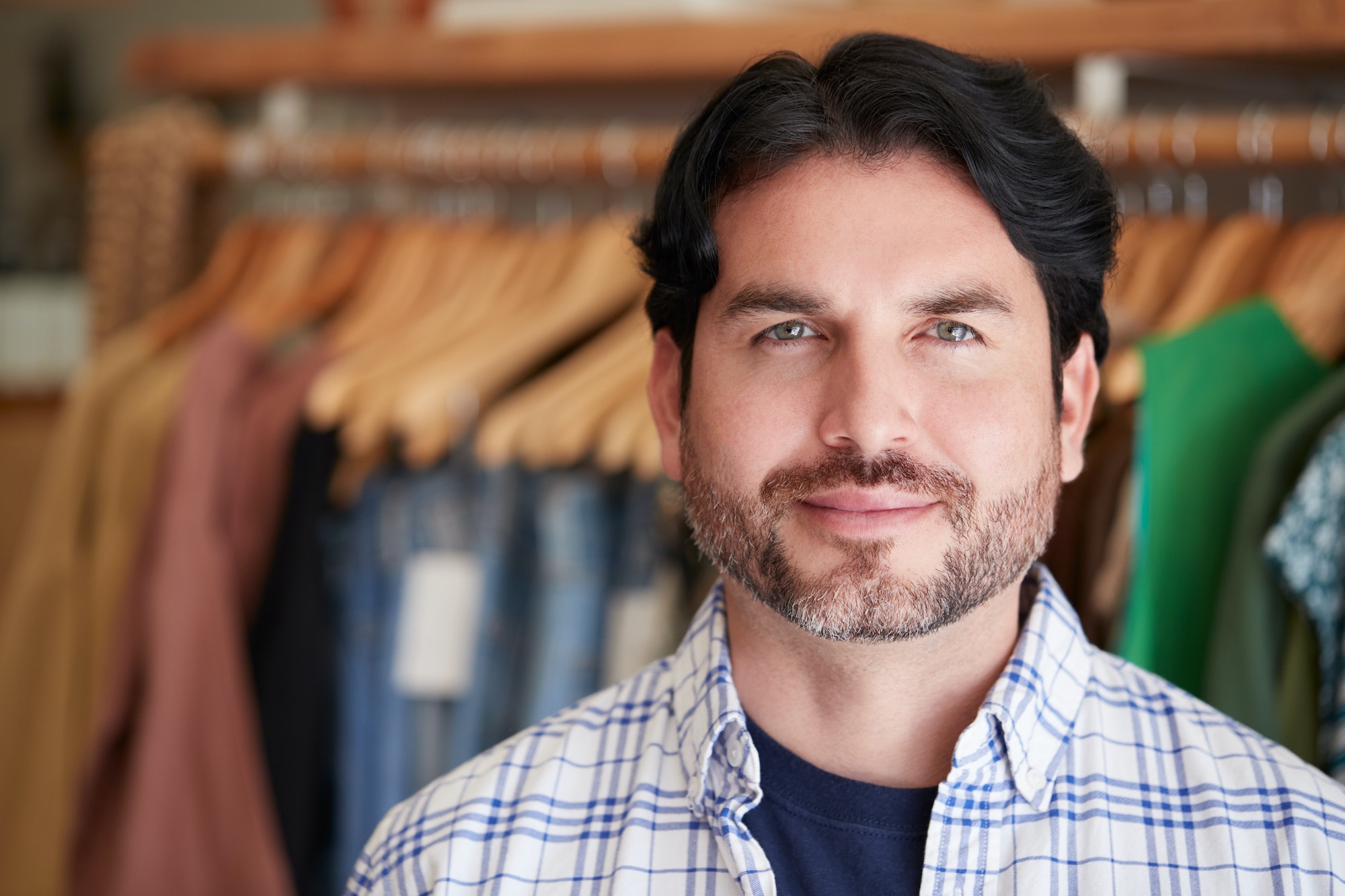 Portrait Of Male Owner Of Fashion Store Standing In Front Of Clothing On Rails