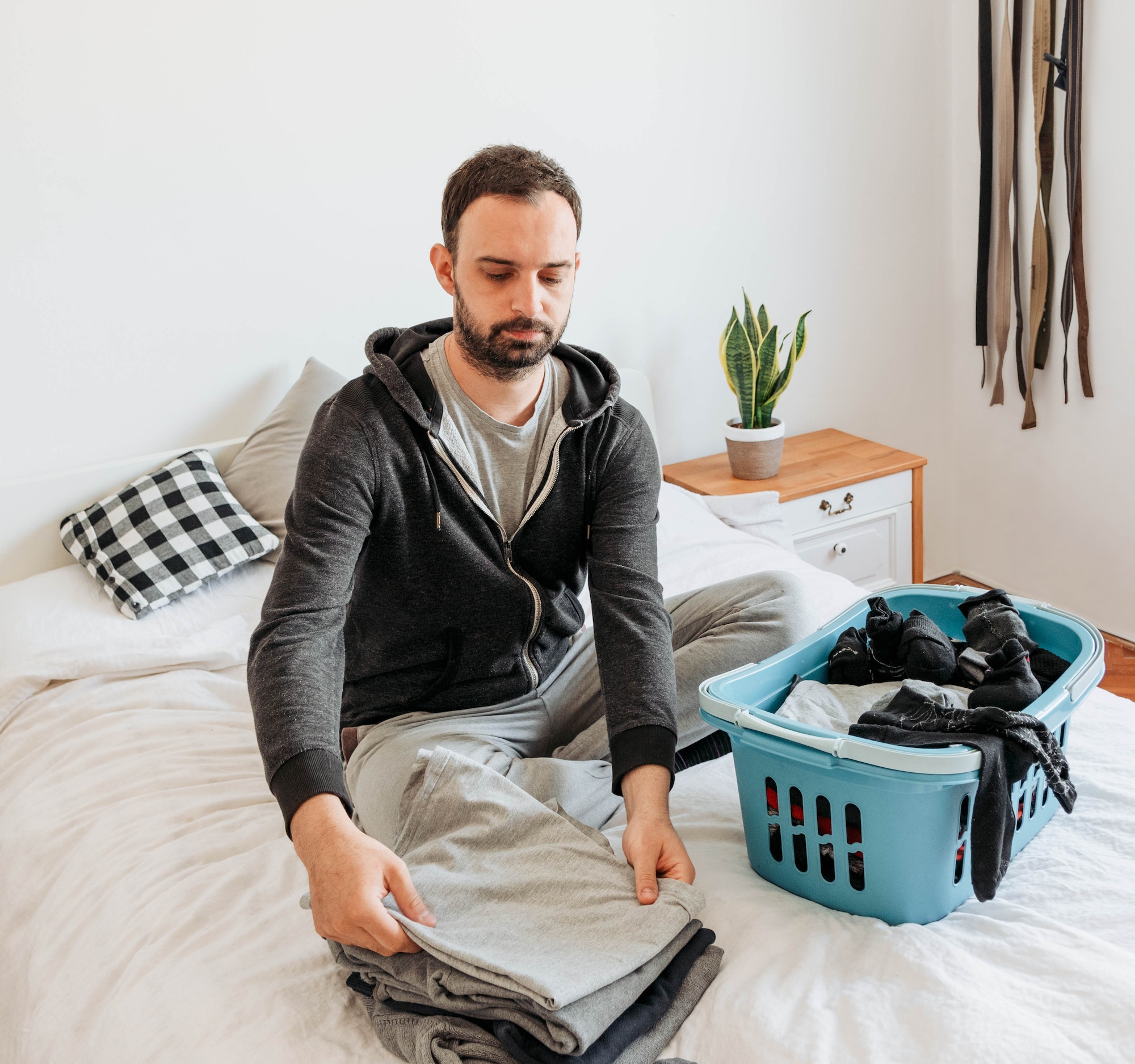 Young man sitting on bed and folding laundry.